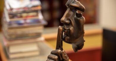 Estátua suspensa com o dedo indicador na boca, simbolizando silêncio e o medo de falar, ilustrando a teoria da Espiral do Silêncio.